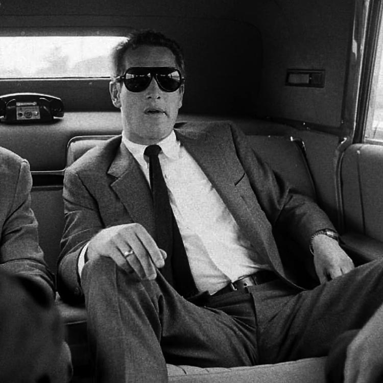 Paul Newman wearing a suit and sunglasses in the back of a car