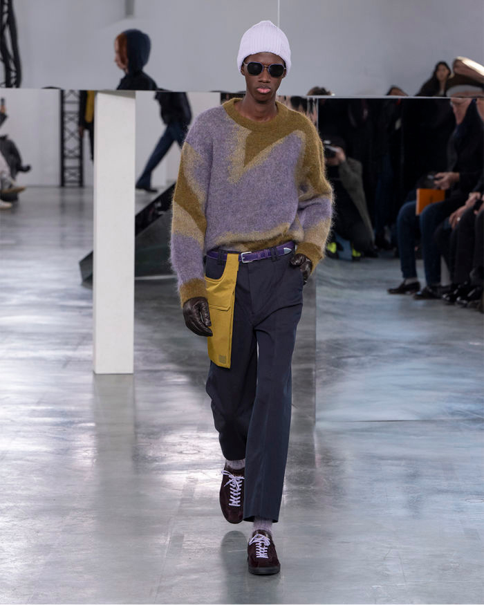 Model walks in a purple jumper and trousers