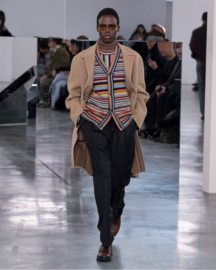 Model walking in a striped cardigan and an overcoat.