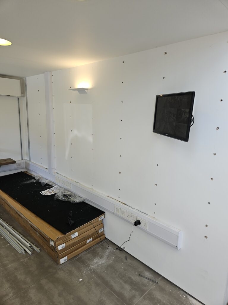 An image of a white wall with holes in and a tv screen mounted to it.