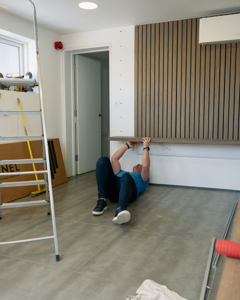 Man lying down on floor screwing shelves into place.