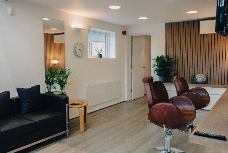 An image of barbershop chairs with a sofa and side table in shot.