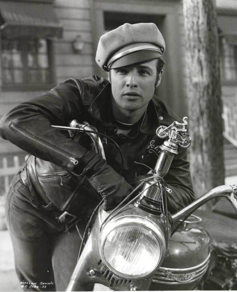 A man posing for a photo leaning across the handlebars of a motorcycle