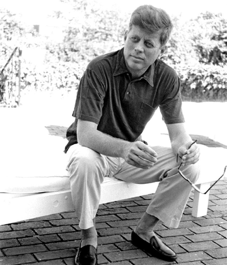 A smartly dressed man sat holding sunglasses