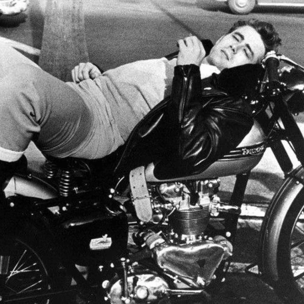 Man lying across a motorcycle whilst smoking.