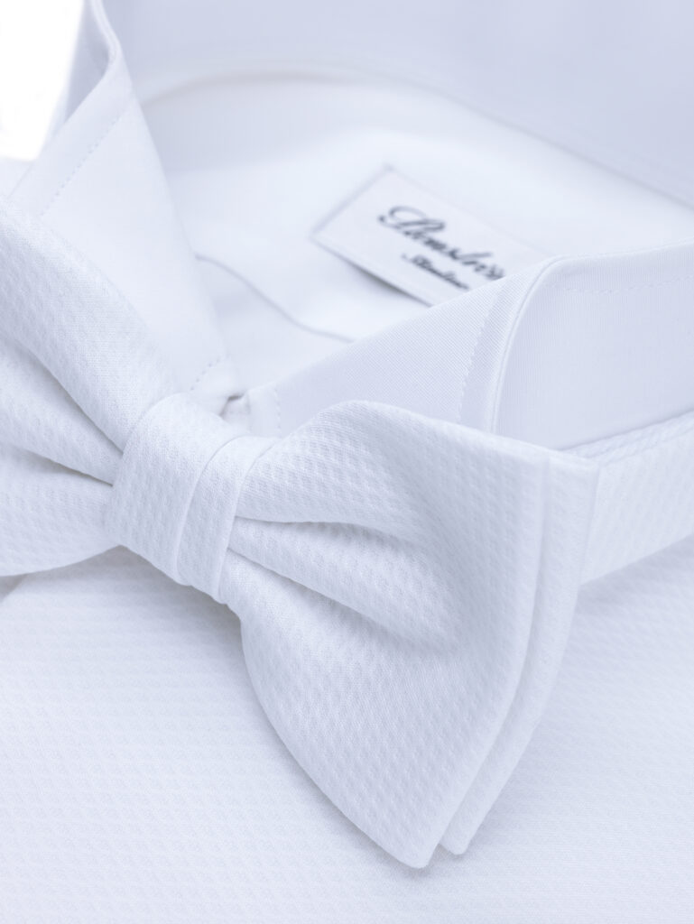 A closeup image of the collar of a smart shirt and white bow tie