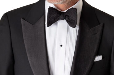 A close-up image of a man's chest wearing a suit with a black bow tie