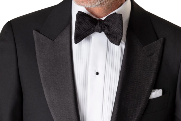 A close-up image of a man's chest wearing a suit with a black bow tie
